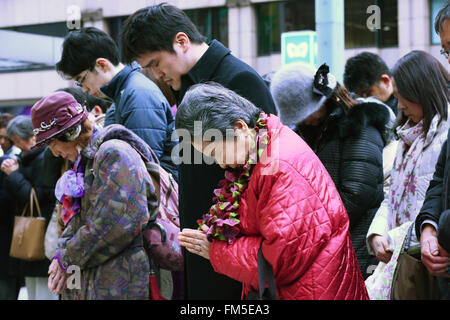 Tokyo, Japan. 11th March, 2016. People take part in a moment of silence at 2:46 pm on the fifth anniversary of the Great East Japan Earthquake and Tsunami disaster at Ginza shopping district on March 11, 2016, Tokyo, Japan. Almost 19,000 people lost their lives as a result of the magnitude 9.0 earthquake and subsequent tsunami that hit Japan's north east coast 5 years ago. Five years after the event some 174,000 survivors are still in temporary accommodation. This includes nearly 100,000 from Fukushima who have not been able to return home as a result of the effects of the tsunami and nuclear  Stock Photo