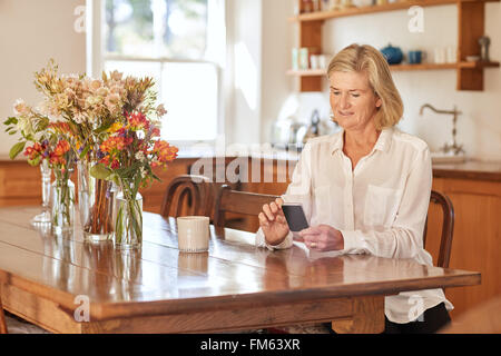 Senior woman reading a message on her phone in kitchen Stock Photo