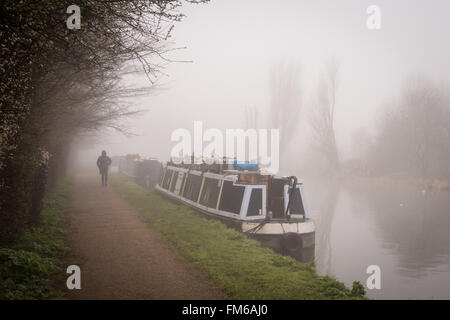 A man walks along the towpath beside some houseboats on a morning of dense fog on the River Lee navigation, Tottenham, London. Credit: Patricia Phillips/Alamy Live News Stock Photo