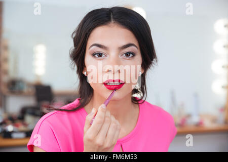 Tender attractive young woman putting on red lipstick with brush Stock Photo