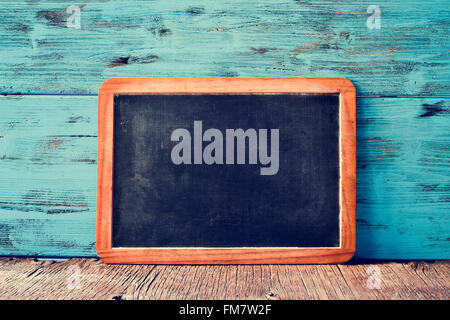 a blank old wooden-framed blackboard on a rustic wooden surface, against a blue rustic wooden background Stock Photo