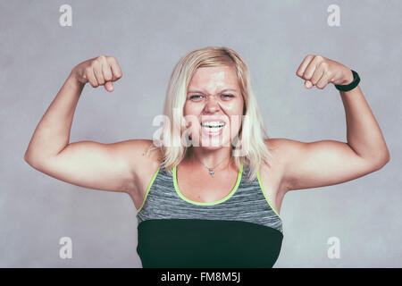 Strong excited muscular woman flexing her muscles. Young blond sporty female showing arms and biceps. Stock Photo