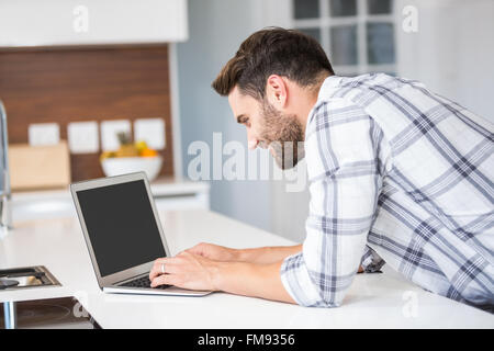 Man using laptop while leaning on kitchen counter Stock Photo