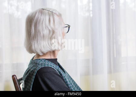 Old lady looking at her window to outdoors Stock Photo