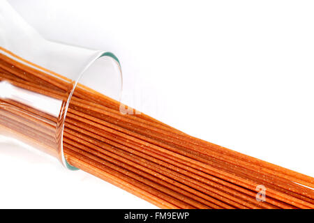 raw brown whole wheat spaghetti in glass jar lying on white background. Stock Photo