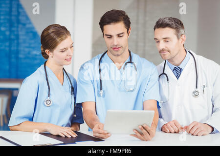 Doctor and colleagues using digital tablet while standing at desk Stock Photo