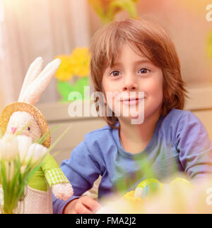Portrait of cute little baby boy sitting in daycare and play with soft bunny toy and colorful eggs Stock Photo