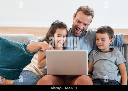 Father sitting with son and daughter and using laptop Stock Photo