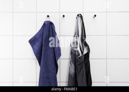 Towel and swimsuit hanging on a white tile wall of a changing room at a swimming bath Stock Photo