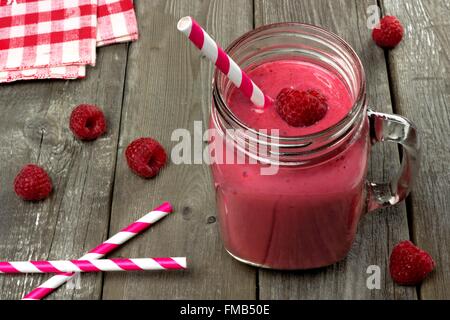Pink raspberry smoothie in a mason jar with straws on a rustic wood background