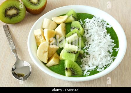 Green smoothie bowl with bananas, fresh kiwi and coconut with spoon on a table Stock Photo