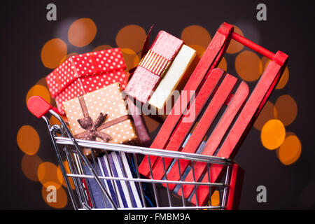 Shooping cart with red sled full of gift boxes on dark background Stock Photo