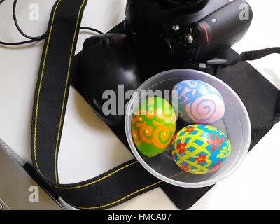 Easter eggs in plastic bowl along side black camera and black mouse on black mouse pad on white tabletop. Easter theme photograp Stock Photo