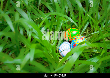 Easter eggs hidden in grass shrub. Homemade, hand painted. Narrow depth of field. Selected focus. Stock Photo