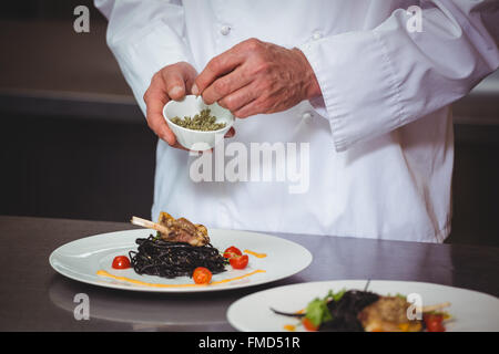 Chef sprinkling spices on dish Stock Photo