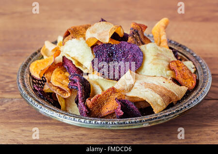 Vintage plate of crunchy vegetable crisps in a vintage silver plate on a wooden table. Stock Photo