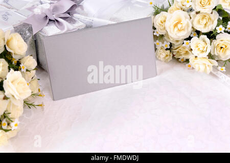 Silver gray envelopes or invitations with several wedding gifts and white rose bouquets laid on white bridal lace. Stock Photo