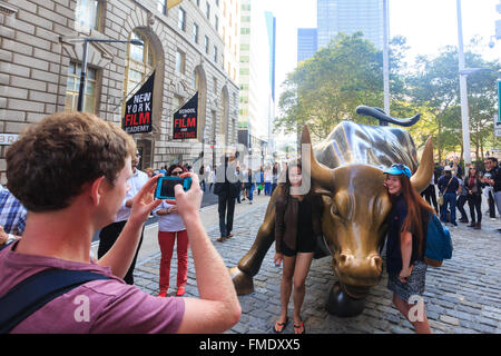 NEW YORK CITY - SEP 16: Charging Bull sculpture and tourists on SEP 16, 2014 in New York City. The sculpture is both a popular t Stock Photo