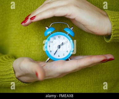 Little blue alarm clock in the hands of woman, the concept of saving time Stock Photo