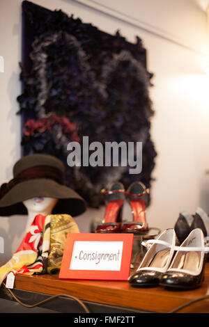 A consignment sign sitting on a shelf in a clothing store surrounded by items for sale. Stock Photo