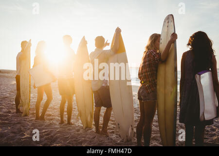 Happy friends standing in line with surfboards