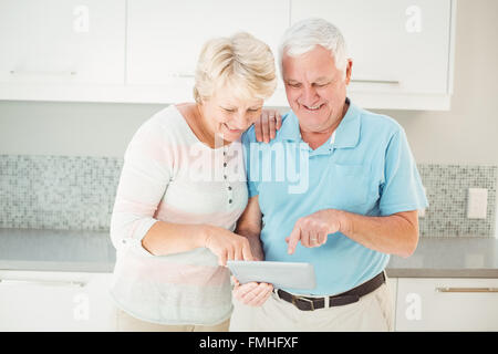 Senior couple laughing using tablet in kitchen Stock Photo