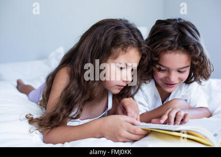 Brother and sister reading book together on bed Stock Photo
