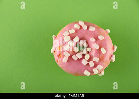 Round ring donut in pink glaze with small marshmallows topping decoration on green paper surface Stock Photo