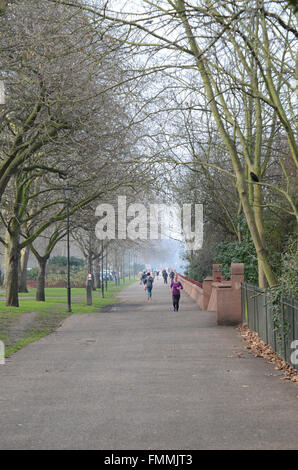 People enjoyed a bright but misty day on and around the Thames in London. The Thames Walk in Battersea Park is popular with joggers Stock Photo