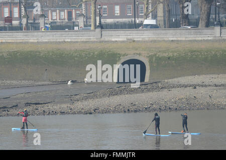 People enjoyed a bright but misty day on and around the Thames in London. Stand up paddle boarders passing outlet at low tide Stock Photo