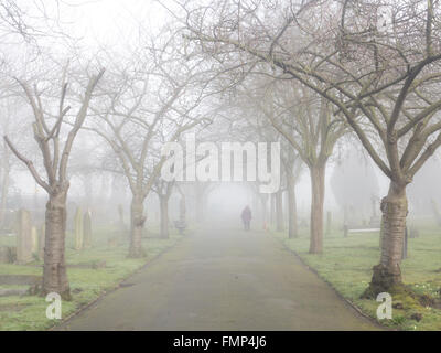 A ghostly figure walks in the fog in a St Mary's graveyard, Wandsworth, London Stock Photo