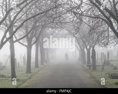 A ghostly figure walks in the fog in a St Mary's graveyard, Wandsworth, London Stock Photo