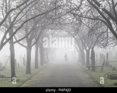 A ghostly figure walks in the fog in a St Mary's graveyard, Wandsworth, London Stock Photo