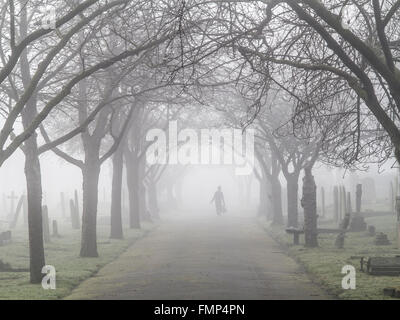 A ghostly figure walks in the fog in a St Mary's graveyard, Wandsworth, London Stock Photo