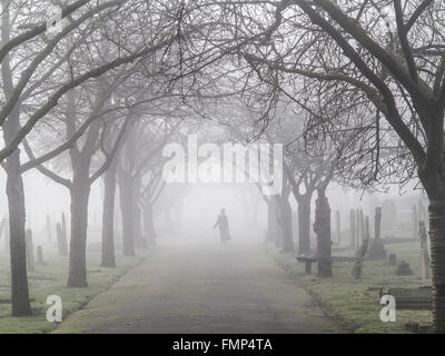 A ghostly figure walks in the fog in a St Mary's graveyard, Wandsworth, London Stock Photo