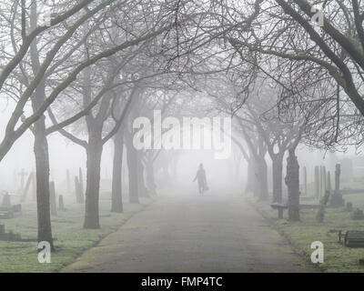 A ghostly figure walks in the fog in a St Mary's graveyard, Wandsworth, London Stock Photo