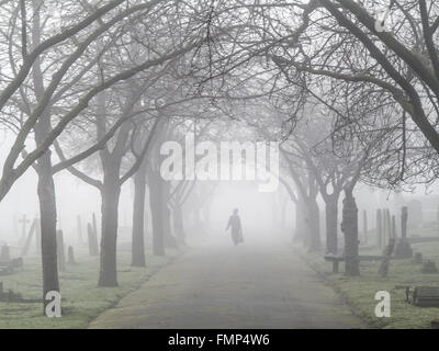 A ghostly figure walks in the fog in a St Mary's graveyard, Wandsworth, London Stock Photo