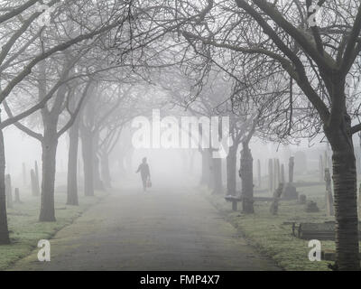 A ghostly figure walks in the fog in a St Mary's graveyard, Wandsworth, London Stock Photo