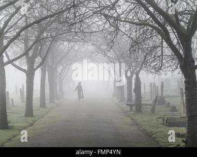 A ghostly figure walks in the fog in a St Mary's graveyard, Wandsworth, London Stock Photo