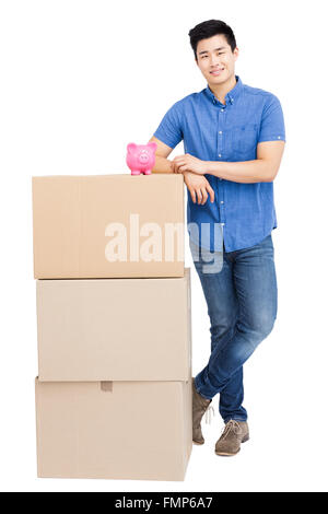 Young man standing near cardboard boxes with piggy bank Stock Photo