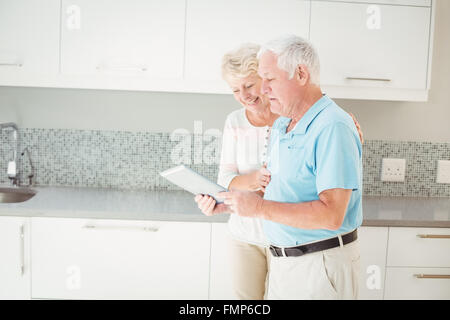 Senior couple laughing while using tablet in kitchen Stock Photo
