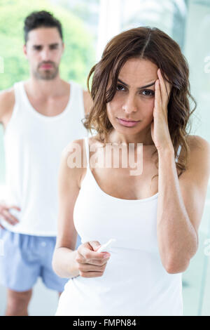 Tensed woman holding pregnancy kit while husband in background Stock Photo