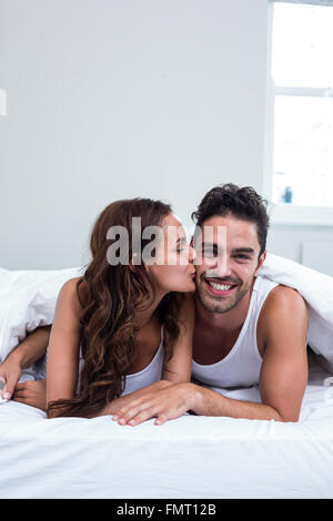Woman kissing man while lying under blanket Stock Photo