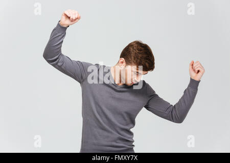 Attractive young man in grey pullover dancing over white background Stock Photo