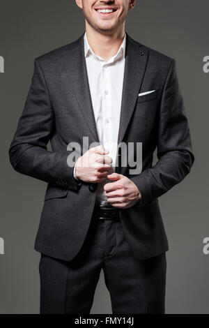 Cheerful attractive young businessman in black suit and white shirt over grey background Stock Photo