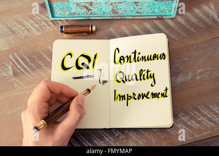 Retro effect and toned image of a woman hand writing a note with a fountain pen on a notebook. Business Acronym CQI as Continuous Quality Improvement as business concept image Stock Photo