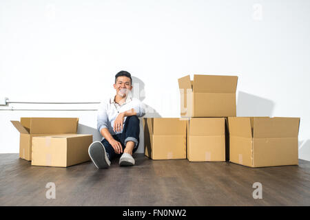 A yong asian man sitting on floor smiling with boxes, moving house Stock Photo