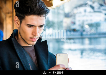 Young dark haired man standing on wooden medieval footbridge in Switzerland taking photo with smartphone Stock Photo