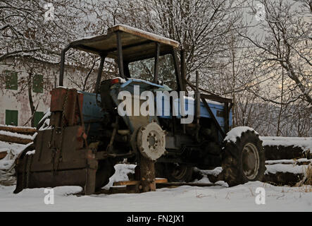 abandoned tractor without a wheel in the snow in winter Stock Photo