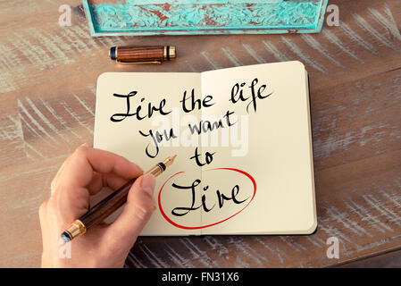 Retro effect and toned image of a woman hand writing a note with a fountain pen on a notebook. Handwritten text Live The Life You Want To Live as business concept image Stock Photo